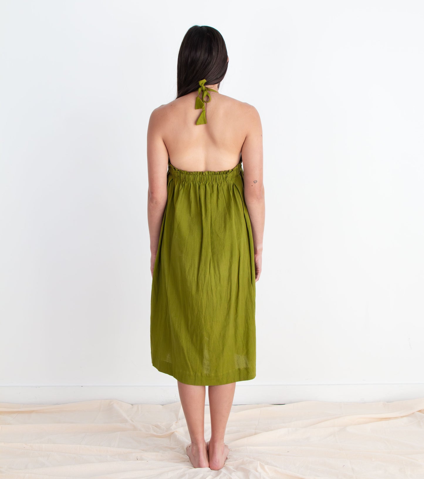 Woman wearing a green dress standing on a white floor with a white wall background