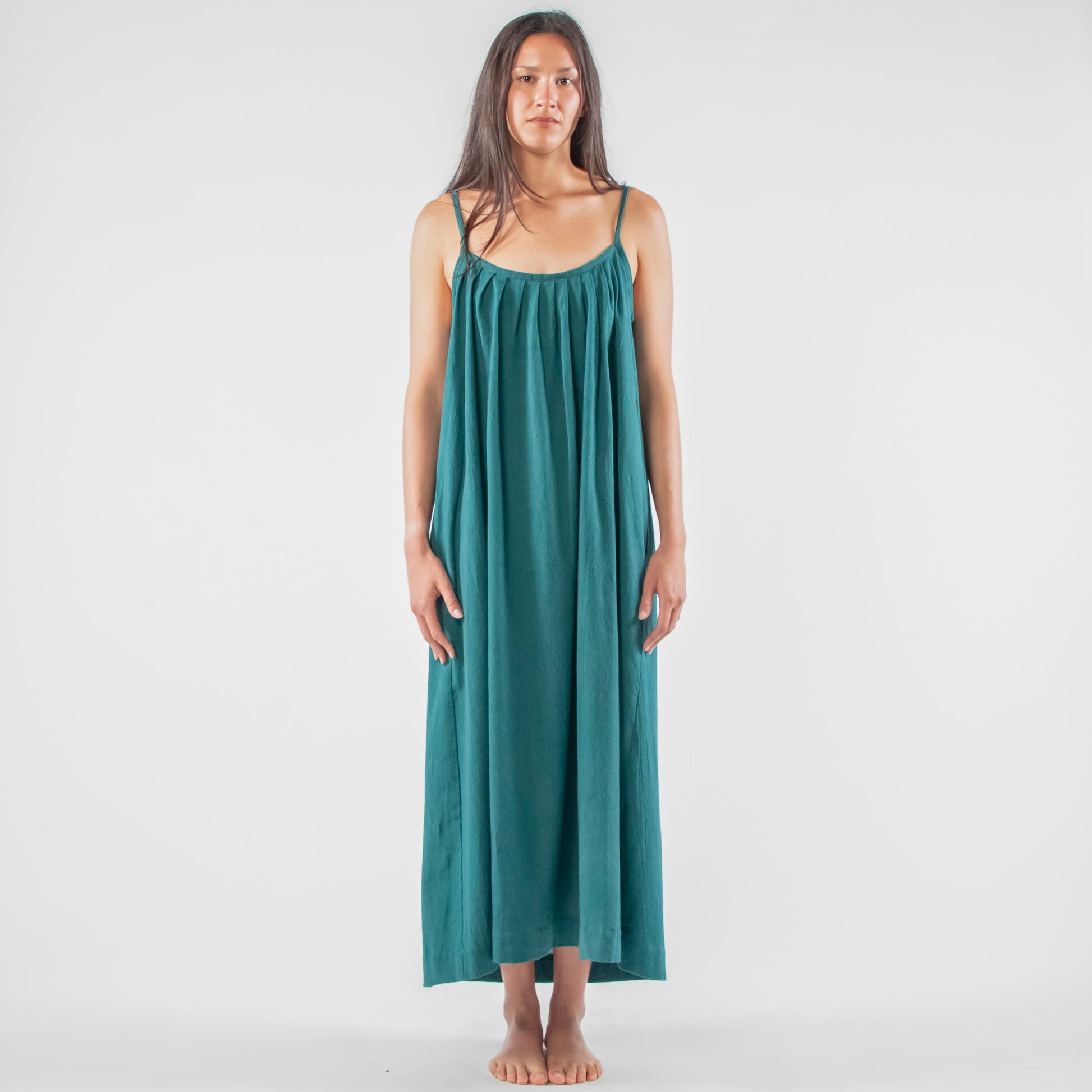 Woman wearing a teal dress standing on a white background with photography equipment around.