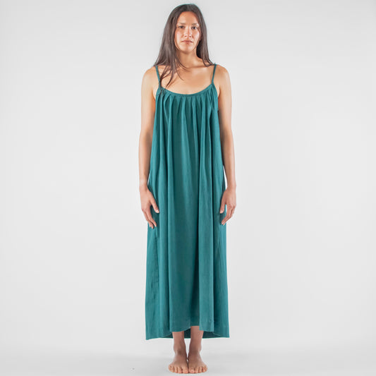 Woman wearing a teal dress standing on a white background with photography equipment around.