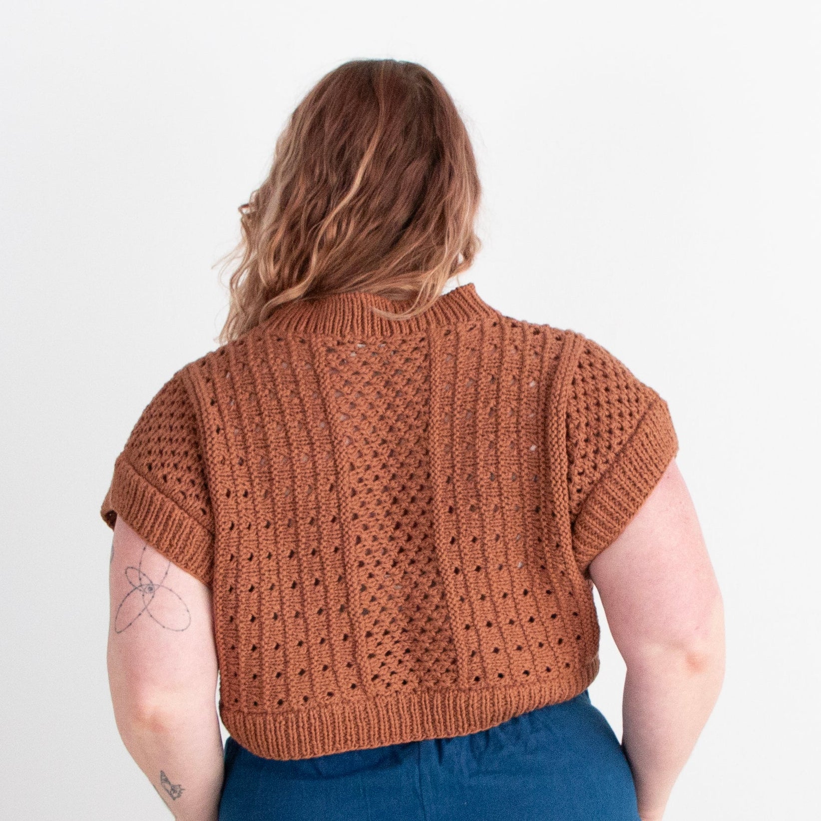 Person wearing a brown knitted sweater and blue pants on a white background
